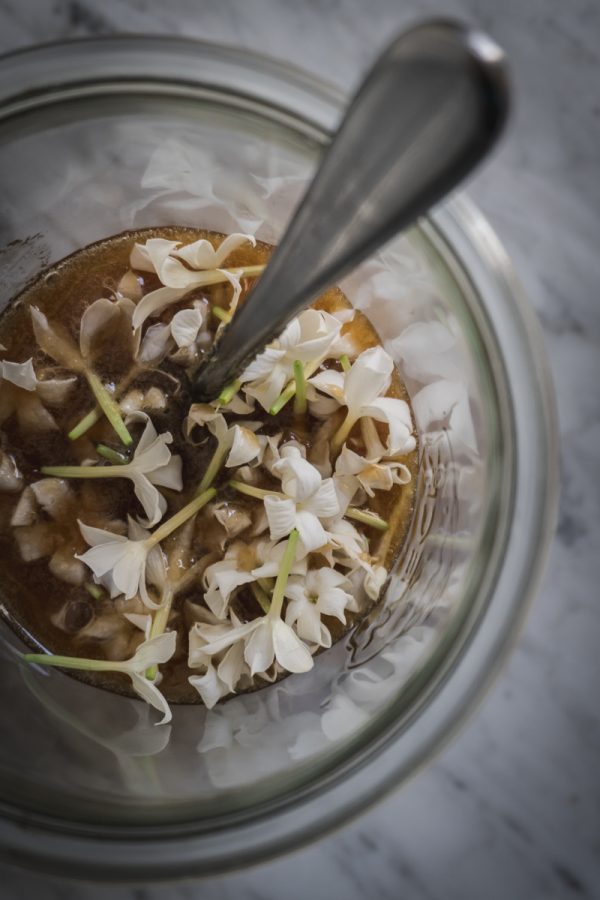 looking into a jar of honey filled with jasmine flowers